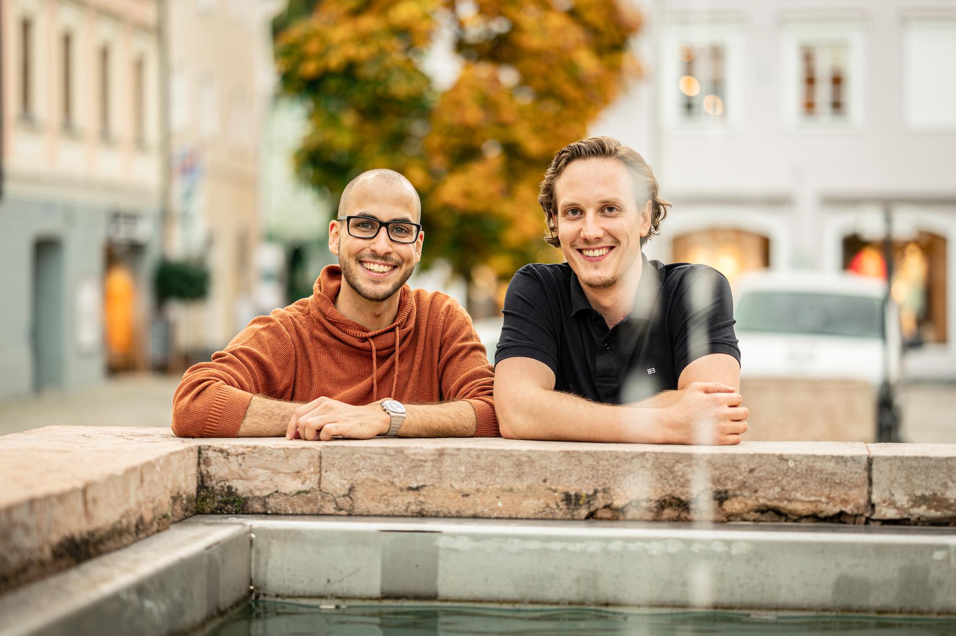 Thomas Steiner und Tobias Franek hinter einem Brunnen stehend mit Blick in die Kamera