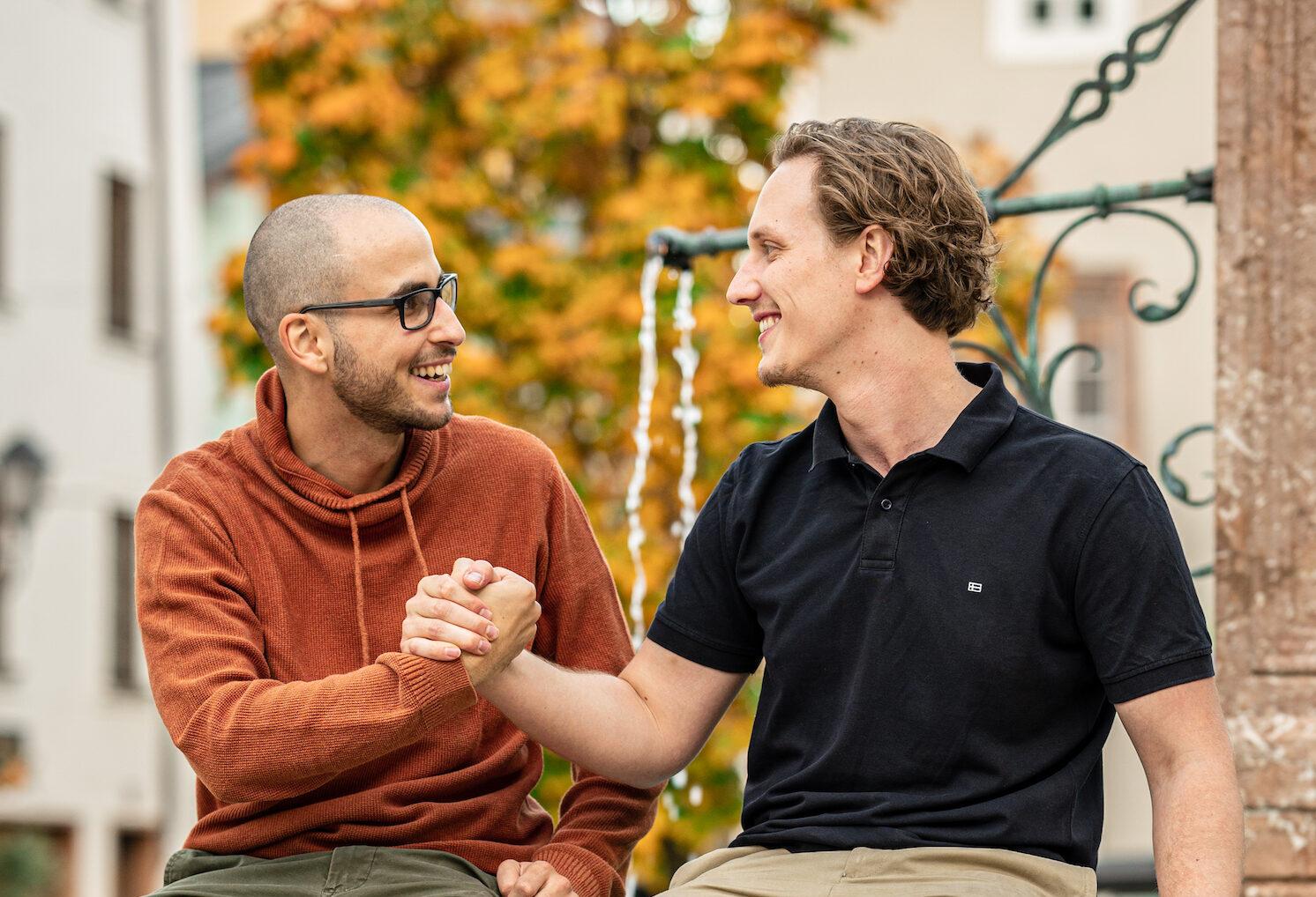 Thomas Steiner und Tobias Franek sitzen auf einem Brunnen bei einem Handschlag